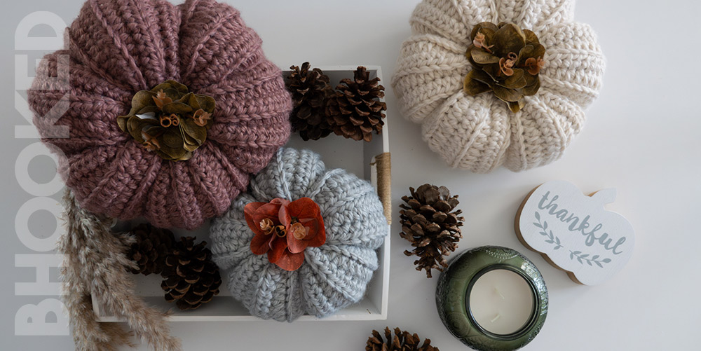 Three perfect crochet pumpkins arranged with pine cones and other fall decor