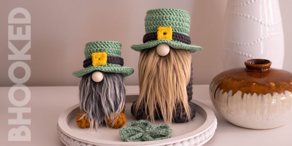 Two St Patricks Day Crochet Gnomes sitting on a table with vases
